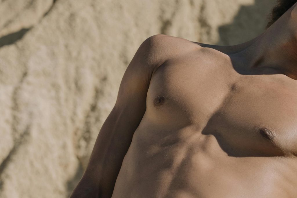 Close-up of a shirtless man's torso with a sandy background.